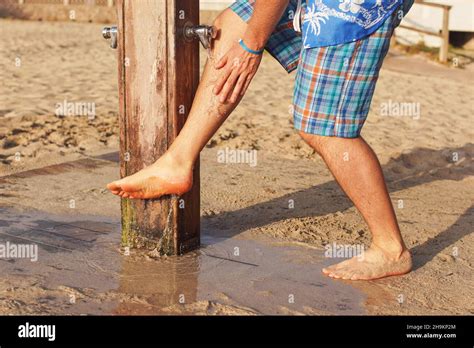 young man  shorts removing sand form  legs  beach shower
