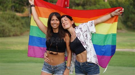 Spanish Lesbian Couple Posing In A Golf Field With A Pride Flag Stock