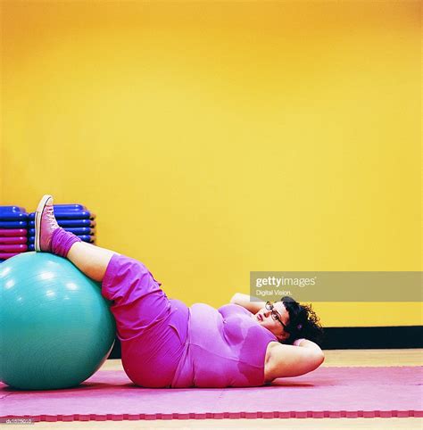 Overweight Woman Doing Sit Ups In A Gym With Her Feet Up On An Exercise