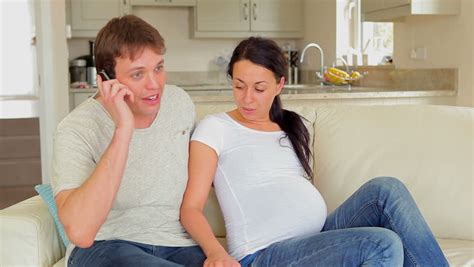 pregnant woman gets contraction on sofa with husband running to help from kitchen stock footage