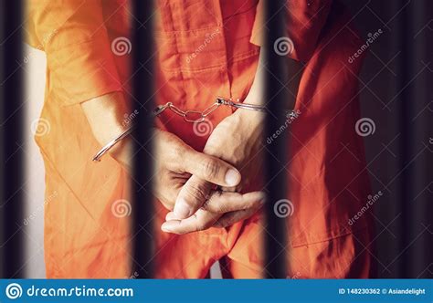 A Prisoner Hands In Handcuffs Behind The Bars Of A Prison In Orange