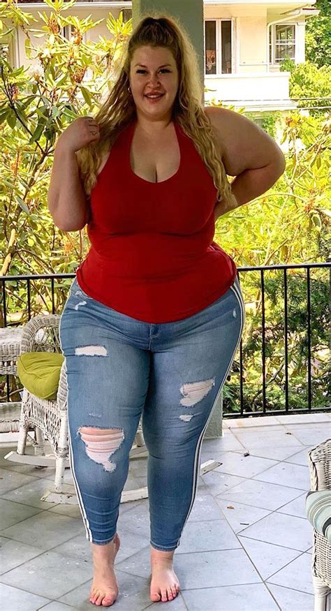 A Woman In Ripped Jeans And A Red Tank Top Standing On A Porch With Her