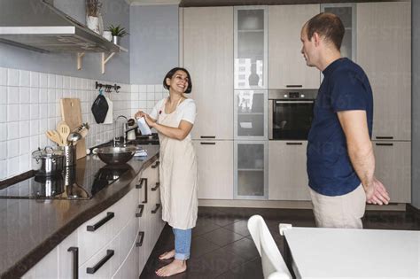 Smiling Wife Talking To Husband While Preparing Food In Kitchen At Home
