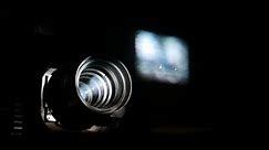 Blurred image on glass, sharp lens, bright beam from cinema projector, dark room. Movie theater details, close up view of beamer device at work, demonstrate some movie