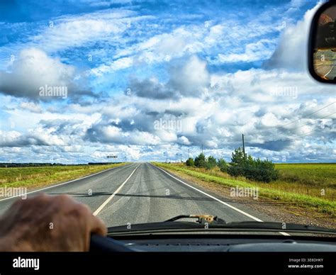 A hand on the steering wheel navigates a wide highway with expansive ...