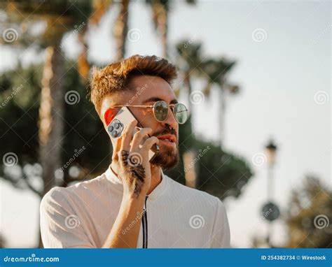 Young Spanish Handsome Man with a Stylish Hairstyle, Tattoos, and Sunglasses Talking on the ...