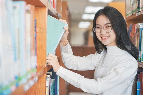 回到学校教育知识学院的大学理念，美丽的女大学生抱着她的书微笑着站在图书馆，学习和教育的理念