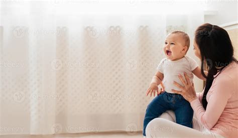 A woman is seated, cradling a baby in her lap. She gazes down lovingly ...