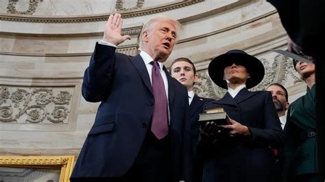 Trump, with his family watching, raises his right hand and places his left hand on the Bible as he t
