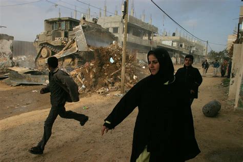 People watch an Israeli army bulldozer demolishing homes in the Palestinian urban refugee camp of Nu