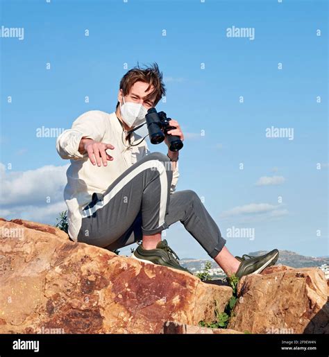 A Spanish adventurous male traveler wearing a mask sitting on a rock ...