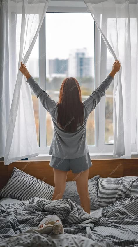 Back view of well rested young asian woman waking up after sleeping standing up from bed and ...