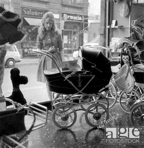 A girl looking at a pram displayed in a shop window. Italy, 1960s ...