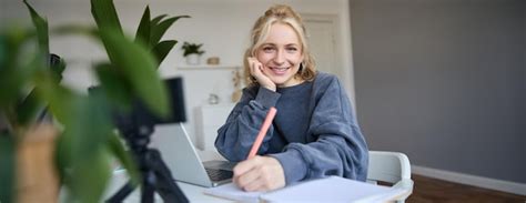Cute smiling girl sits in a room writes down notes doing homework ...