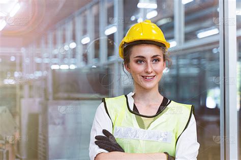 手工女工的肖像正自信地站在高科技清洁工业工厂的玻璃墙前，穿着蓝色的工作服和绿色的安全帽。智慧产业工作