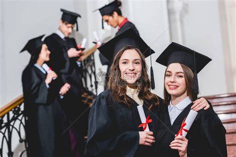 戴着毕业帽的漂亮女孩在学生附近拿着文凭时微笑高清图片下载-正版图片502616246-摄图网