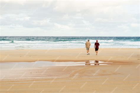 Rear view of two friends walking and talking on a beach with the ocean ...