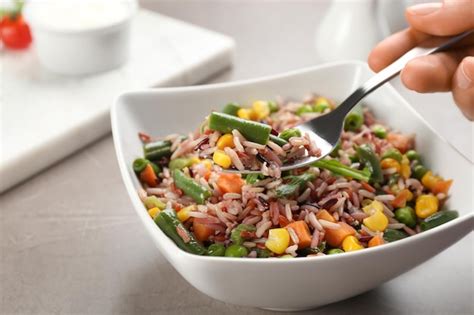 Woman eating tasty brown rice with vegetables at grey table closeup ...