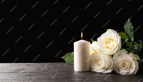 Beautiful white roses and candle on table against black background ...