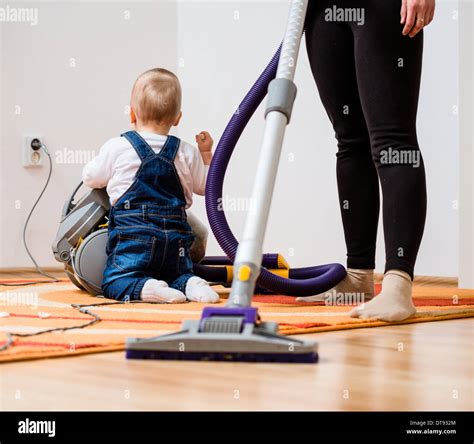 Cleaning up the room - woman with vacuum cleaner, baby sitting on floor ...