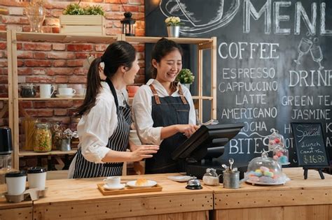 Azjatycka baristka mówiąca coś zabawnego koledze podczas pracy. dwie ...