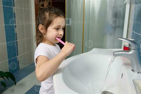 Beautiful preschooler little girl brushing teeth, standing by sink in ...