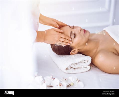 Beautiful brunette woman enjoying facial massage with closed eyes in ...