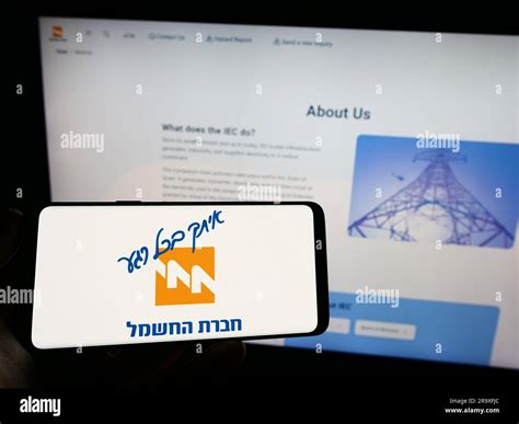 Person holding mobile phone with logo of utility company Israel Electric Corporation (IEC) on ...