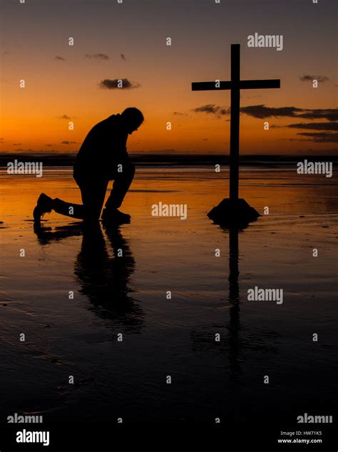 Cross with a man kneel in prayer on a beach at sunset Stock Photo - Alamy