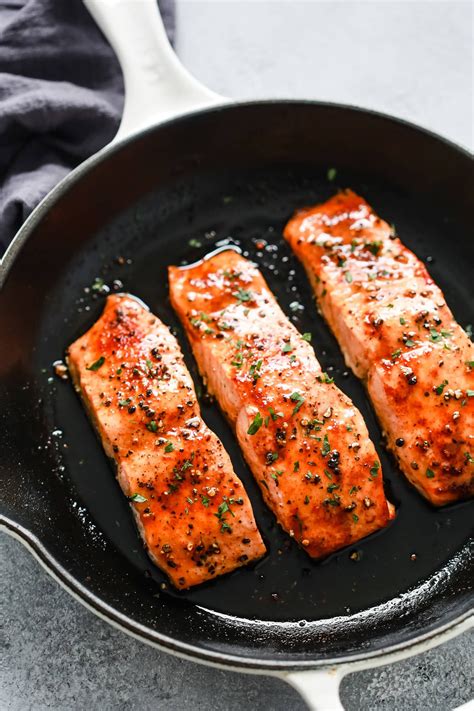 three salmon fillets in a skillet with seasoning on top, ready to be cooked