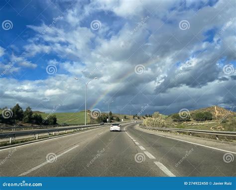 A White Car Driving Around a Curve on a Freeway through the Rainbow Coming Out of the Storm on a ...