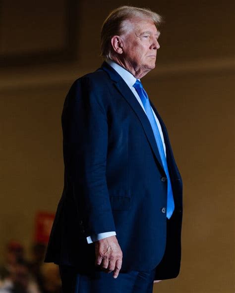 US President Donald Trump, wearing a dark blue suit, white shirt, and light blue tie, looks ahead, h