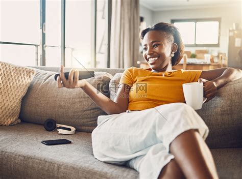 轻松、无忧无虑、微笑的年轻女性在家客厅沙发上看电视和流媒体电影。高清摄影大图-千库网