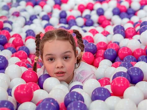 Une petite fille se penche sur des balles en plastique colorées dans ...