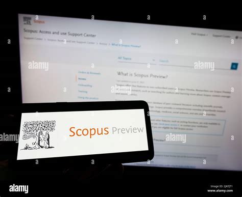 Person holding mobile phone with logo of citation database Scopus Preview on screen in front of ...