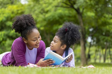 African American mother is teaching her young daughter to read while lying down after having a ...