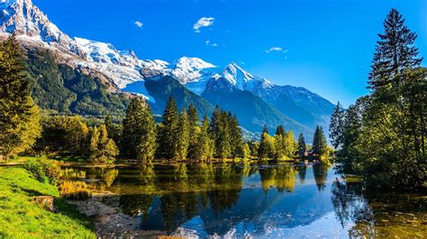 The lake reflects the forest and the blue sky in Chamonix City Park at ...
