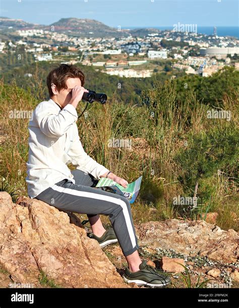 Adventurous young Spanish male traveler sitting on a rock using ...