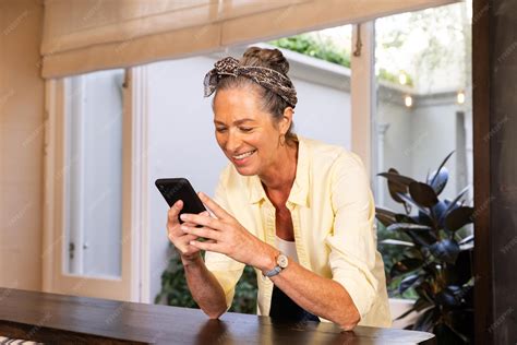 Mulher sênior sorridente usando smartphone enquanto se inclina sobre a ...