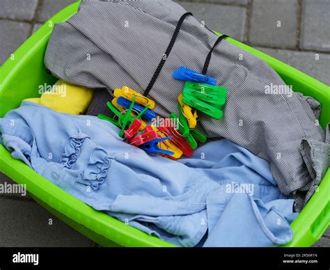 A green laundry basket with clean dried clothes and clothes pins in it ...
