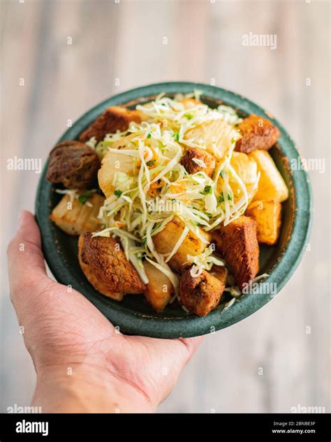 Hand holding a bowl of a delicious traditional Yuca Con Chicharron ...