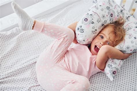 Lying down on the bed. Cute little girl in casual clothes is indoors at home at daytime 15291652 ...