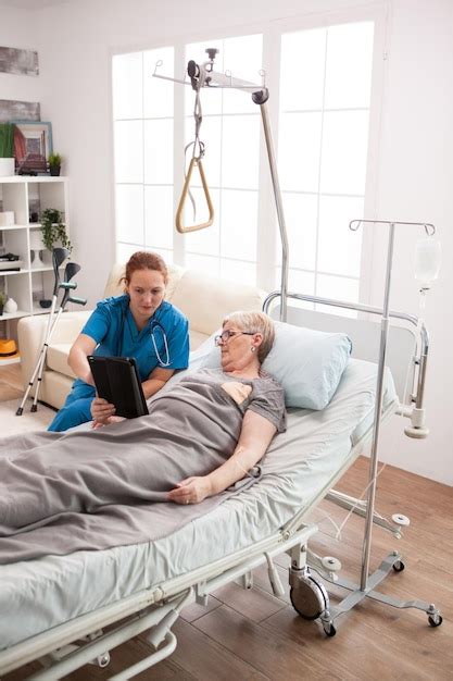 Female caretaker and senior woman using tablet computer in nursing home ...