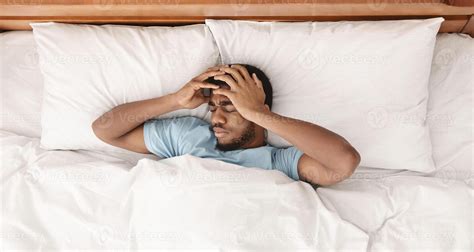 Restless african american man waking up with headache, lying in bed early in morning, top view ...