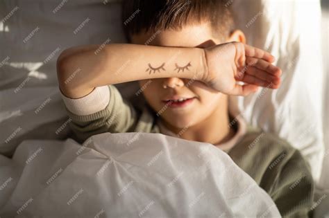Premium Photo | Cheerful cute tired little boy lies on bed puts his ...