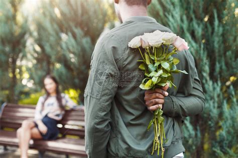 年轻男人背着鲜花在公园约会的美丽女友身边拿着鲜花的高清图片下载-正版图片505177288-摄图网