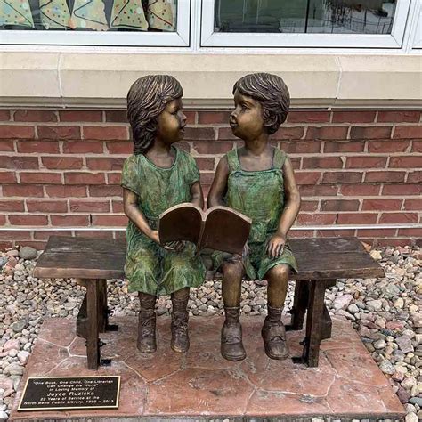 Colored outdoor statue of a child pressing their forehead on the hand of a seated elder