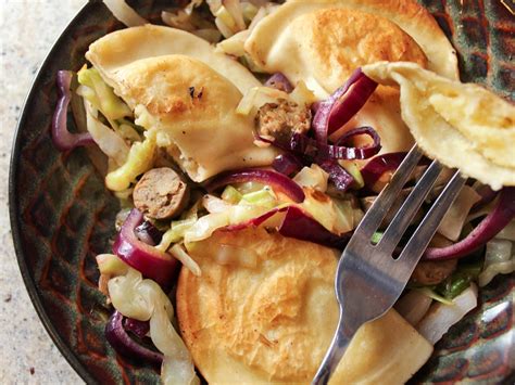 A plate with pierogies sausages and cabbage served with a small bowl of sour cream