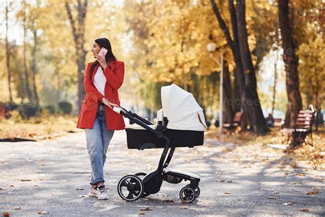 Talking by the phone. Mother in red coat have a walk with her kid in ...