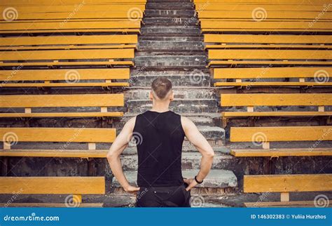 A Slender Young Man in Black Sportswear Stands in Front of the Stairs Stadium Stands. Ready for ...